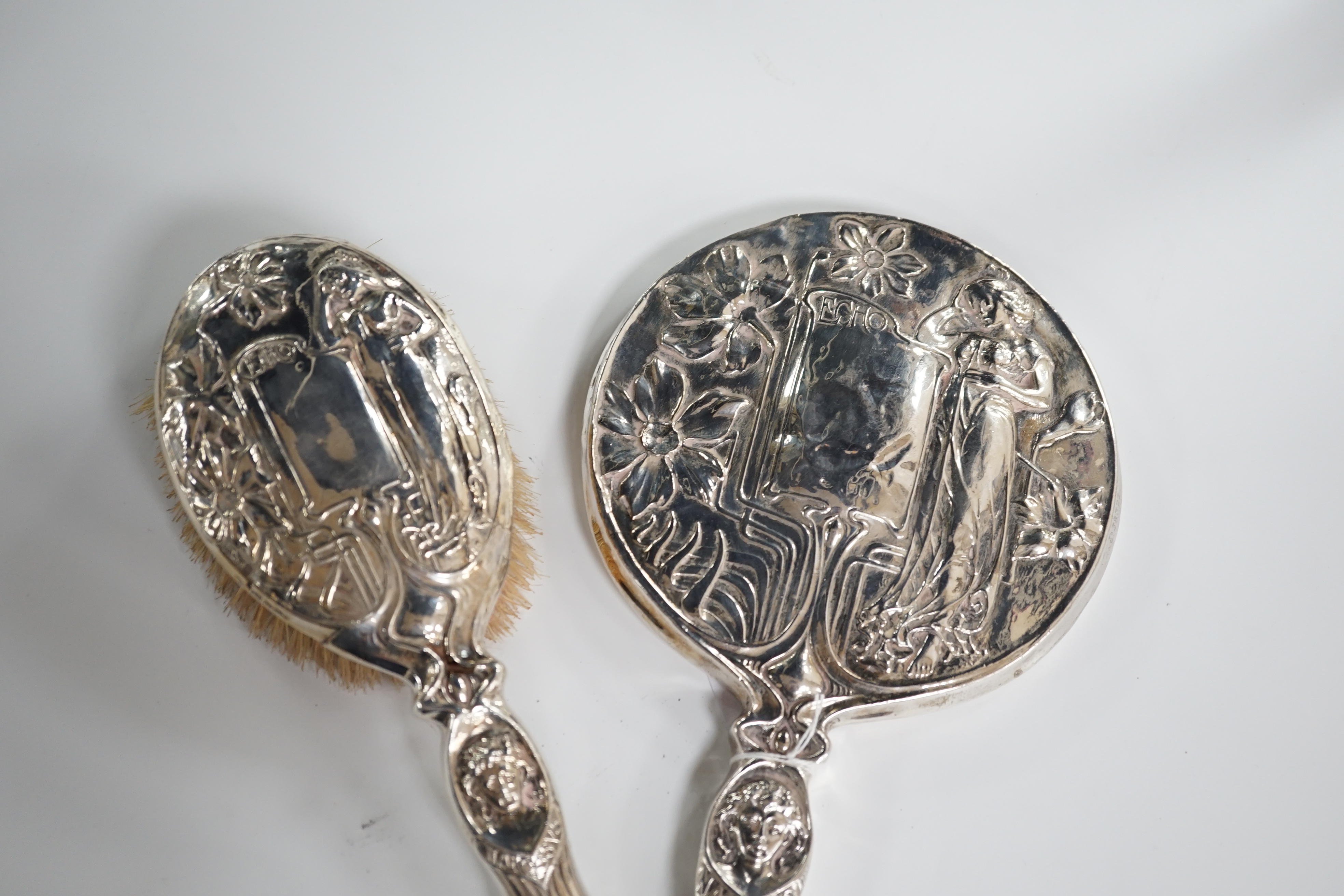 A late Victorian Art Nouveau silver mounted hand mirror, marks rubbed, 27.8cm. and a later similar hair brush, London 1902. Condition - poor